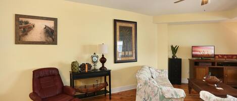 A living room with a brown leather chair, floral sofa, wooden floor, ceiling fan, and a television on a wooden stand.