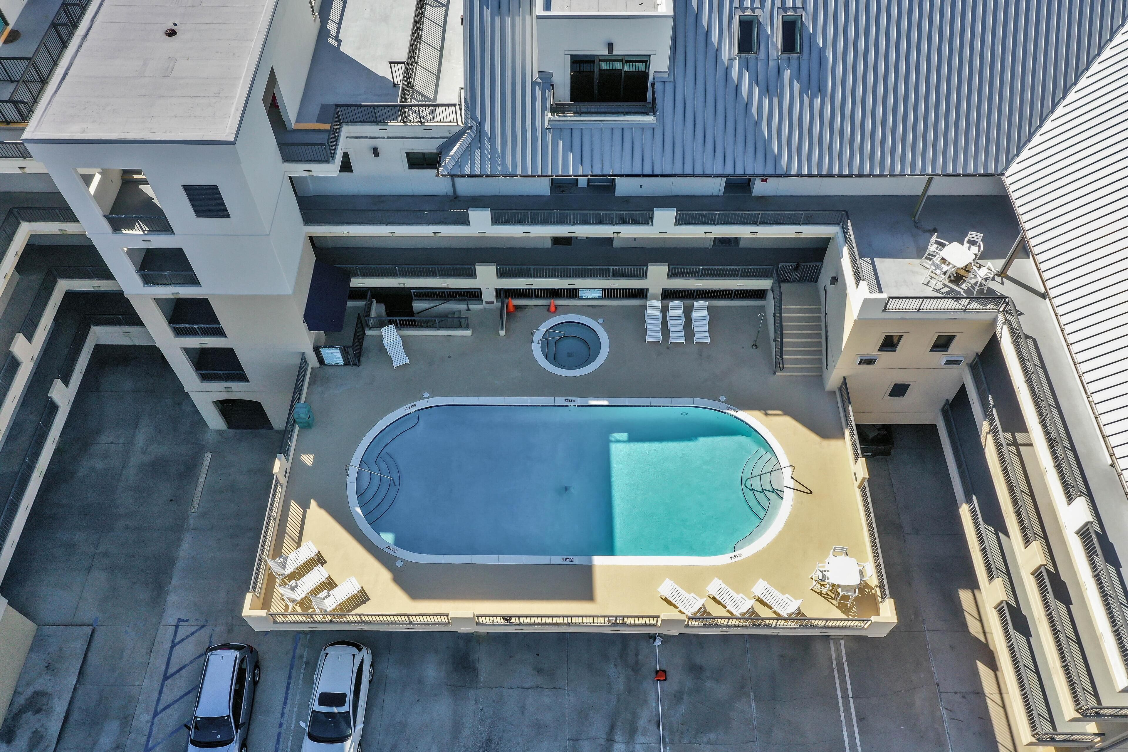 Et luftfoto af en moderne bygning med swimmingpool på taget, flere altaner og en parkeringsplads.