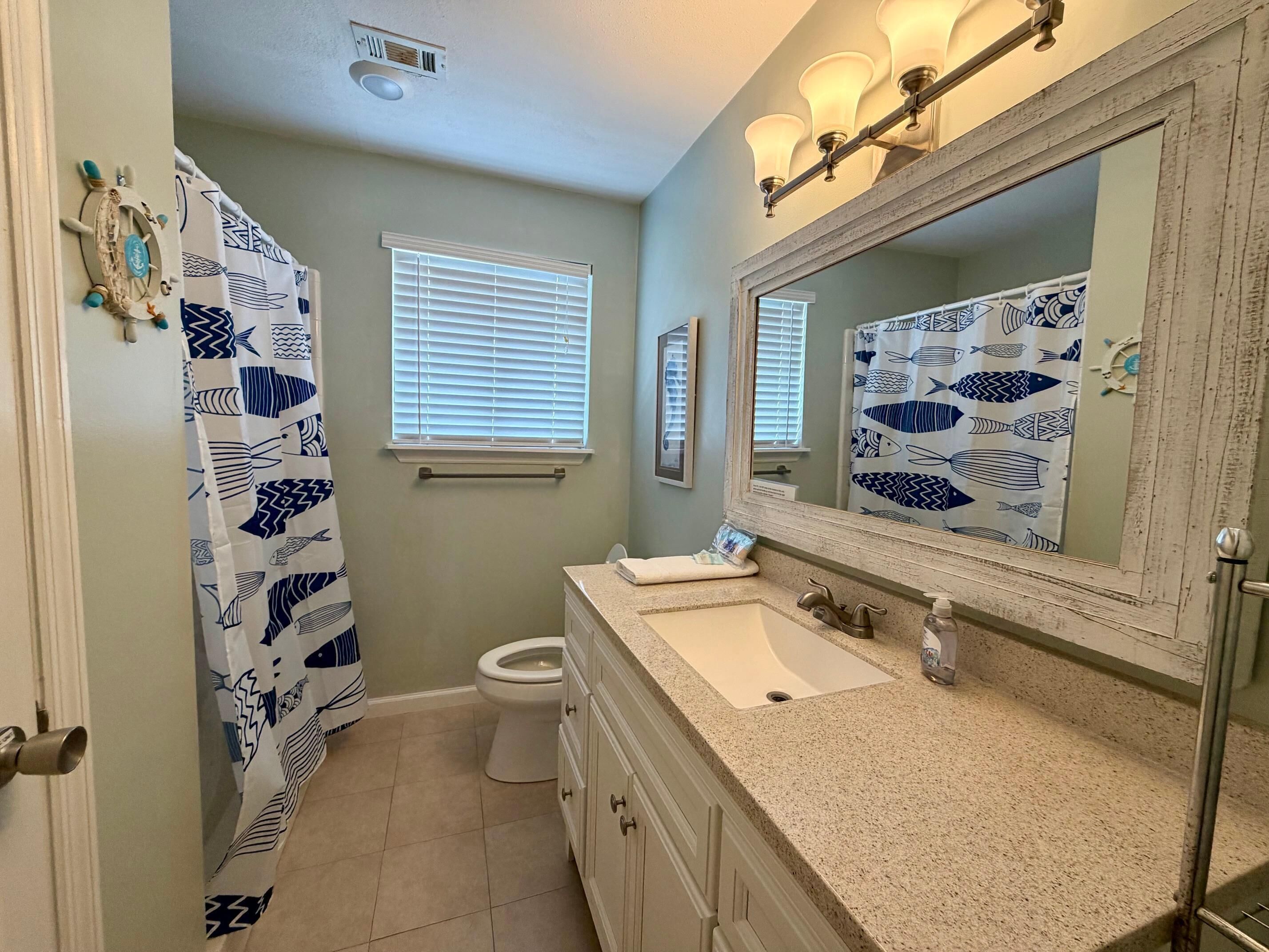 A bathroom with a sink, toilet, and a mirror with a fish pattern backsplash.