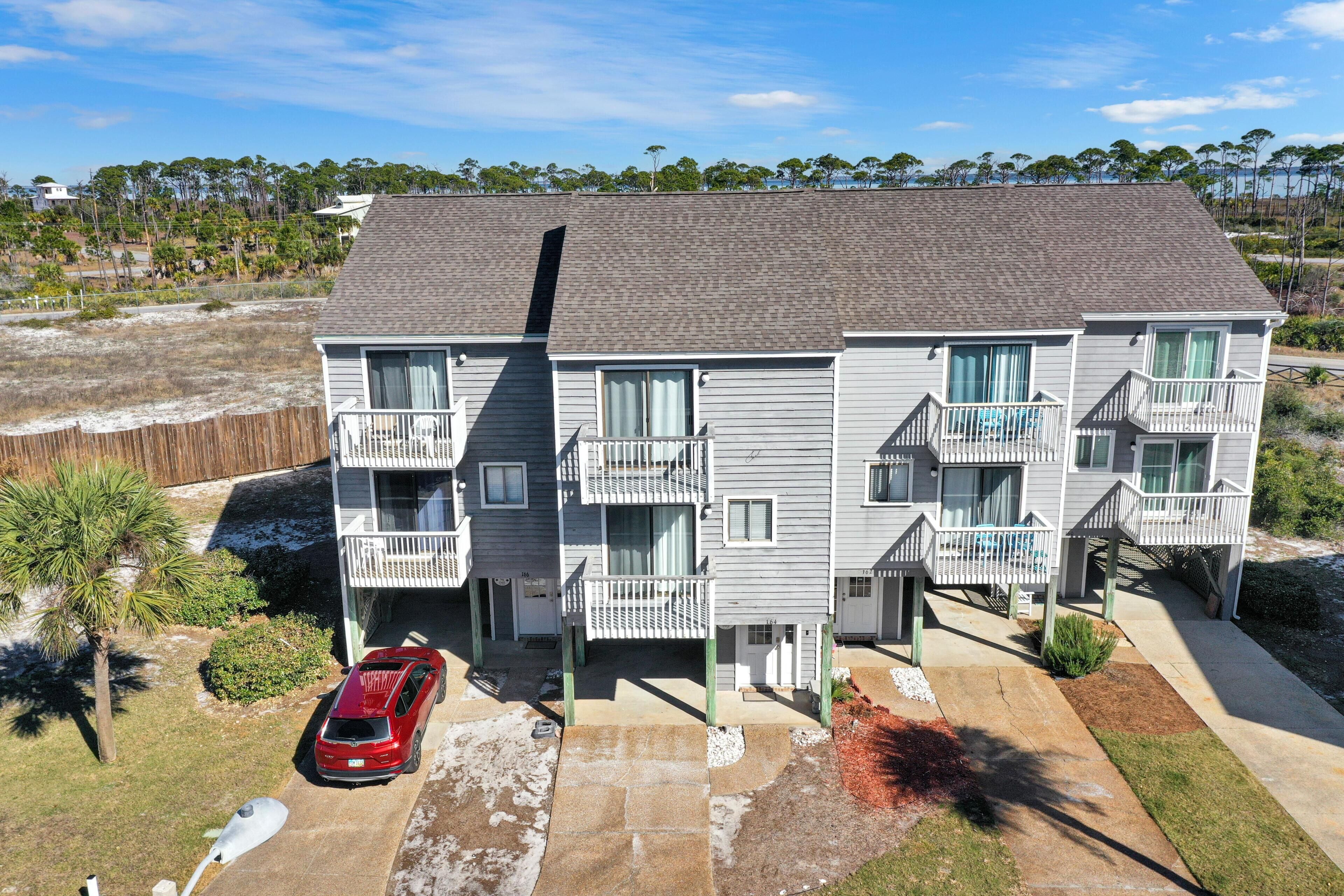 A multi-story residential building with balconies, a driveway, and a red car parked in front.