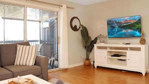 A living room with a sofa, a television, a white entertainment unit, and a sliding glass door. - Barrier Dunes 164 - 144 Bay Breeze (Port St. Joe)