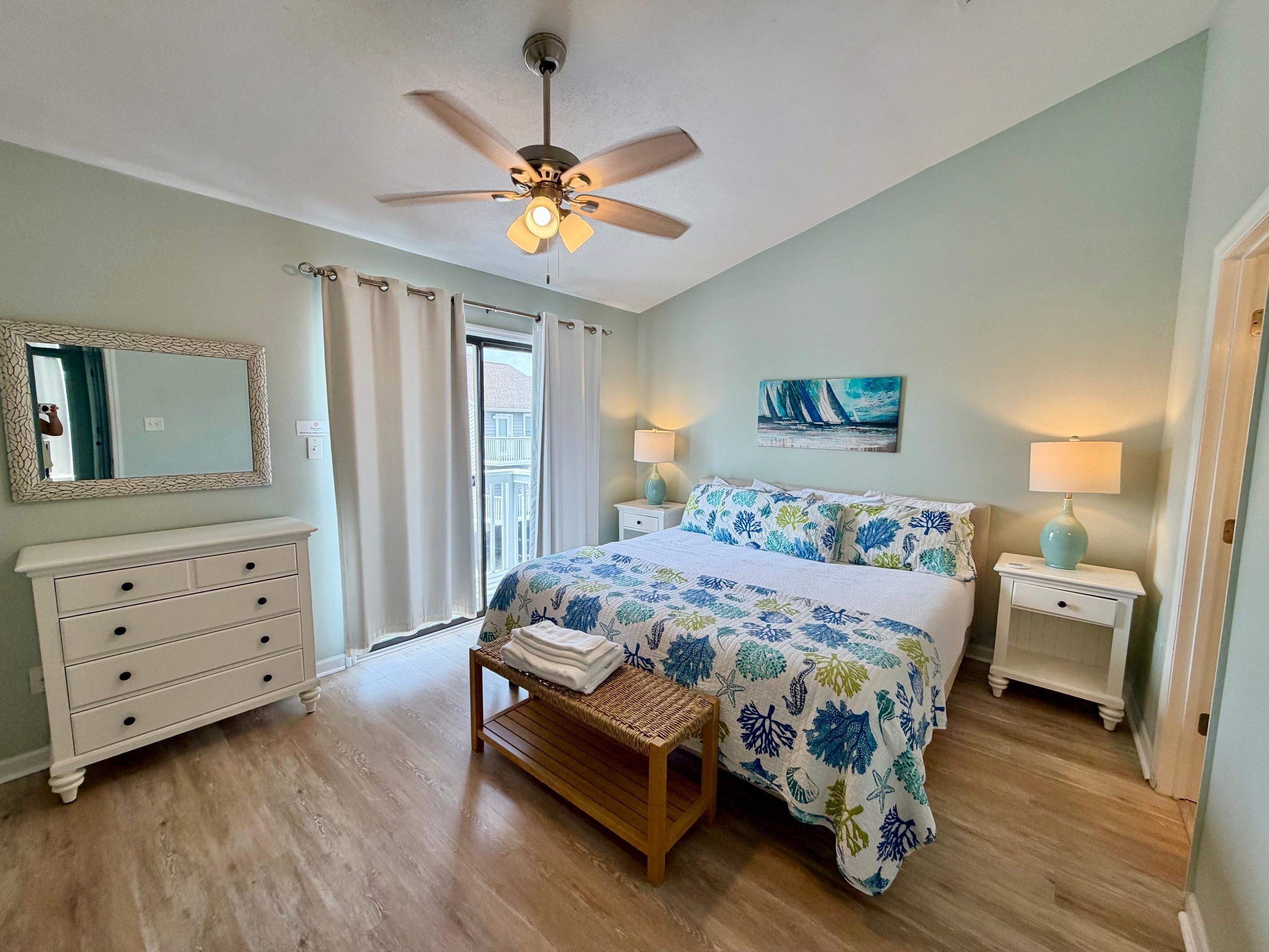 A bedroom with a bed, a nightstand, a dresser, a ceiling fan, and a window with curtains.