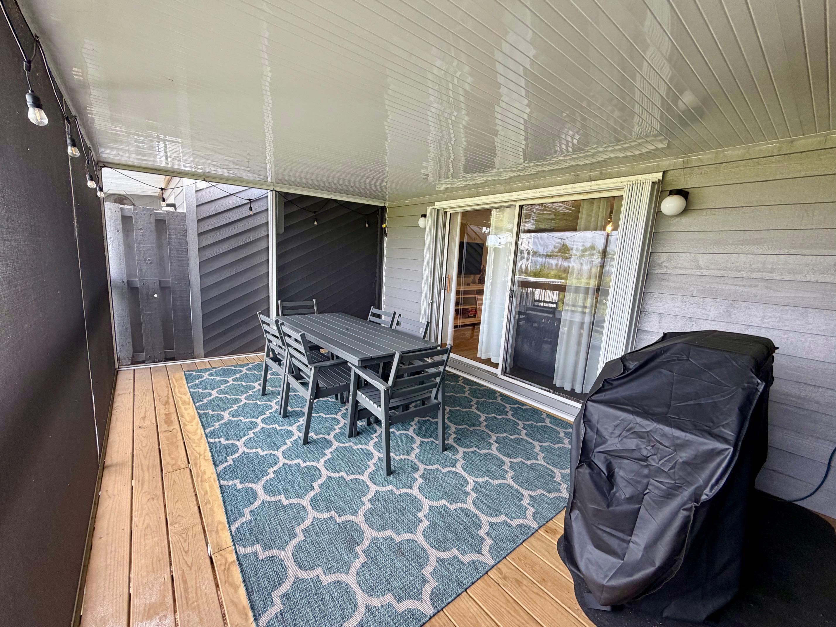A covered patio area with a table and chairs, a patterned rug, and a covered grill.