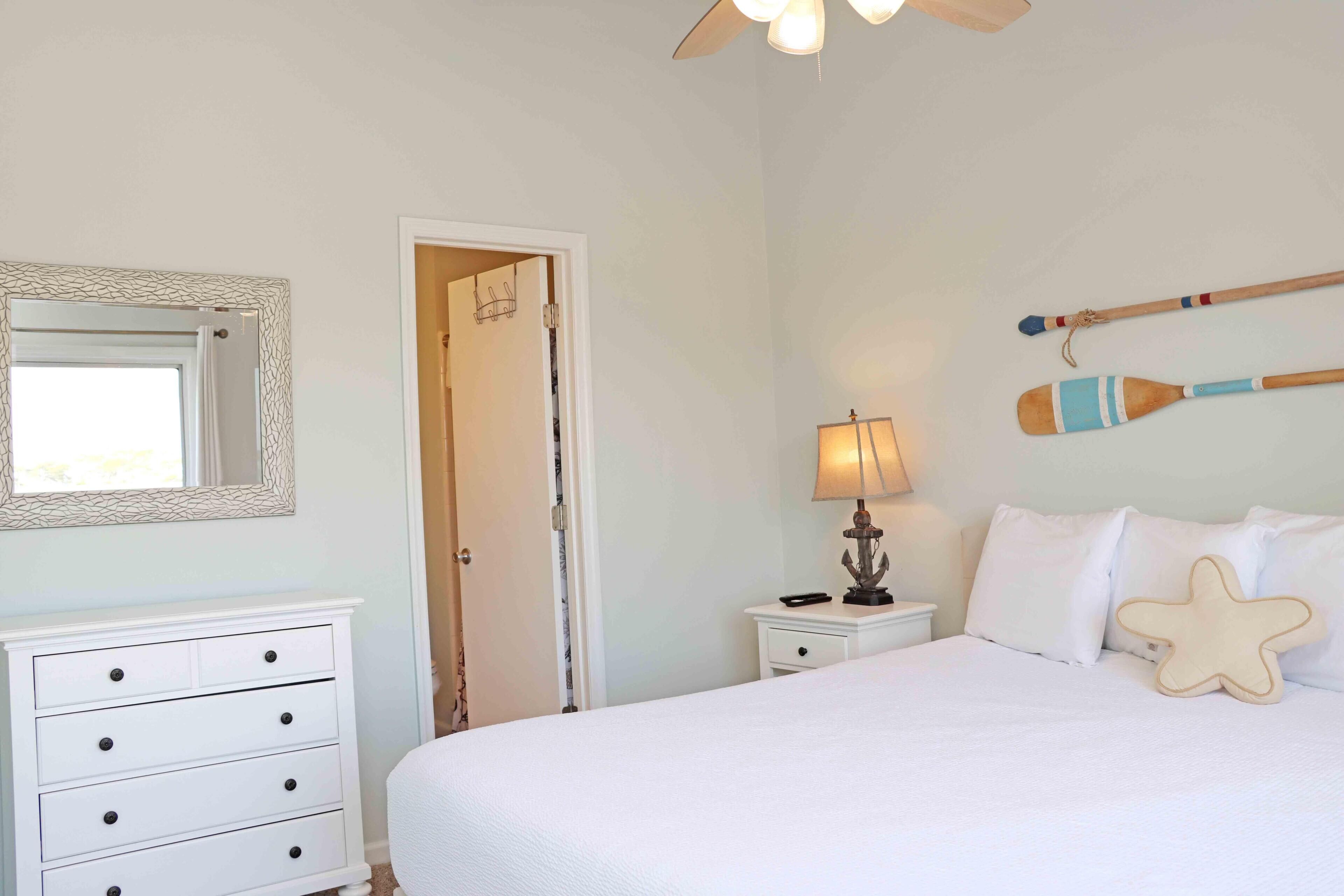 A bedroom with a bed, a dresser, a nightstand, a lamp, a starfish pillow, and a wall-mounted paddle.
