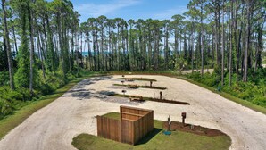 Un camping con camino de tierra, mesas de picnic, una estructura de madera y una playa al fondo.