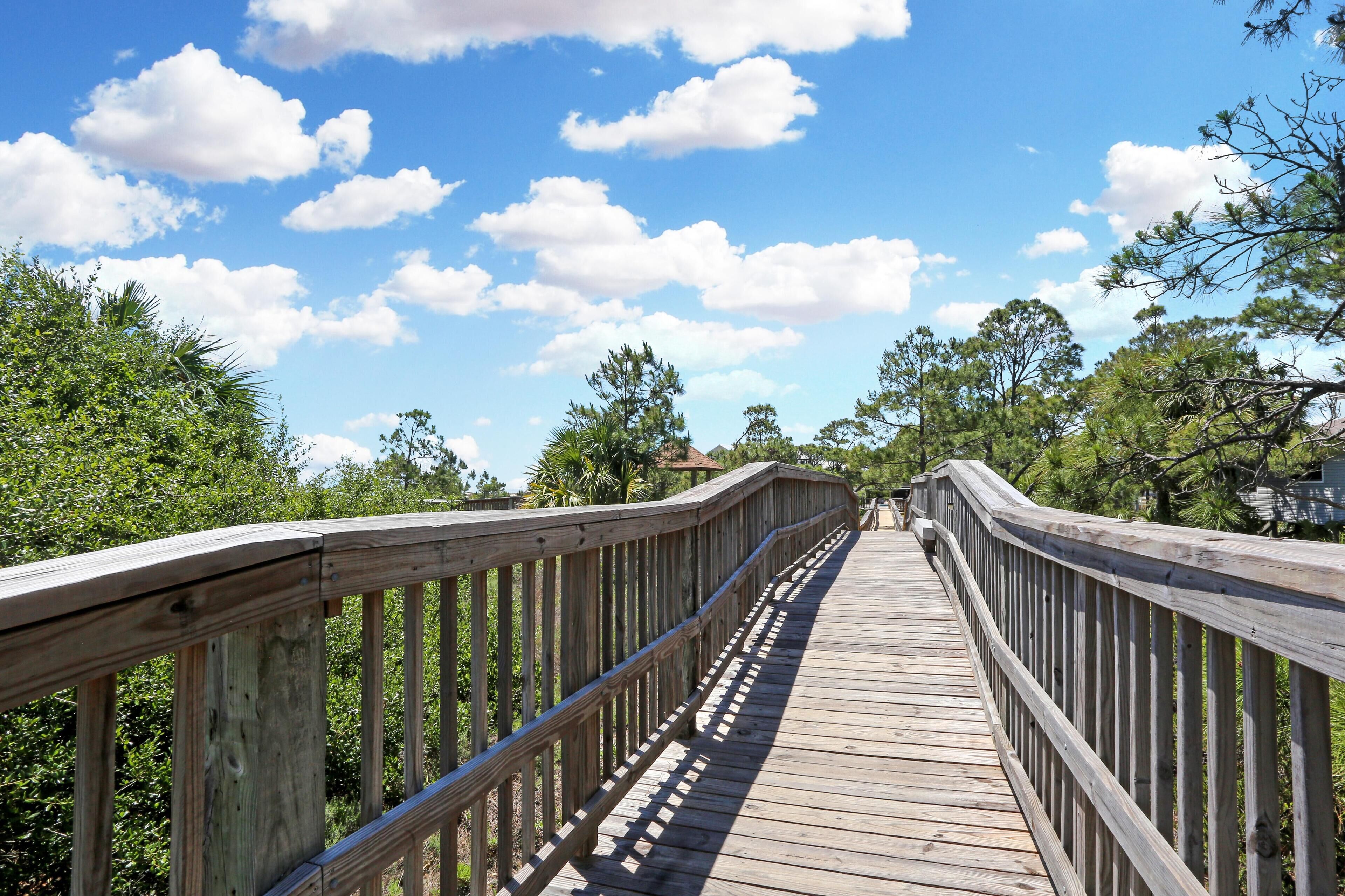A wooden boardwalk leading through a park with trees and a clear sky.