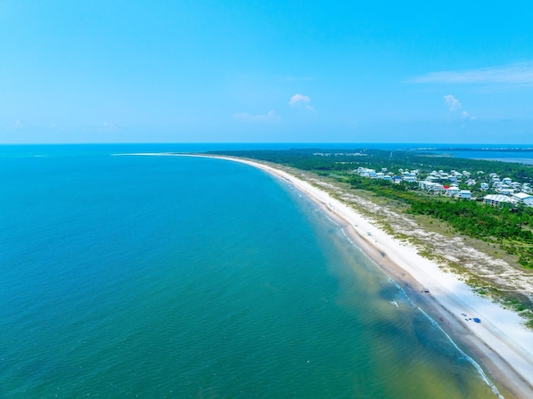 An aerial view of a coastal area with a beach and a residential area with houses.