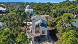 A two-story house with a balcony, surrounded by pine trees and a clear sky. - A Swell Life (Port St. Joe)