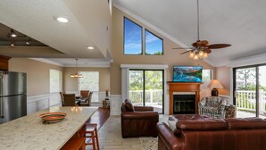 A spacious living area with a fireplace, leather seating, and a large window overlooking a deck. - A Swell Life (Port St. Joe)