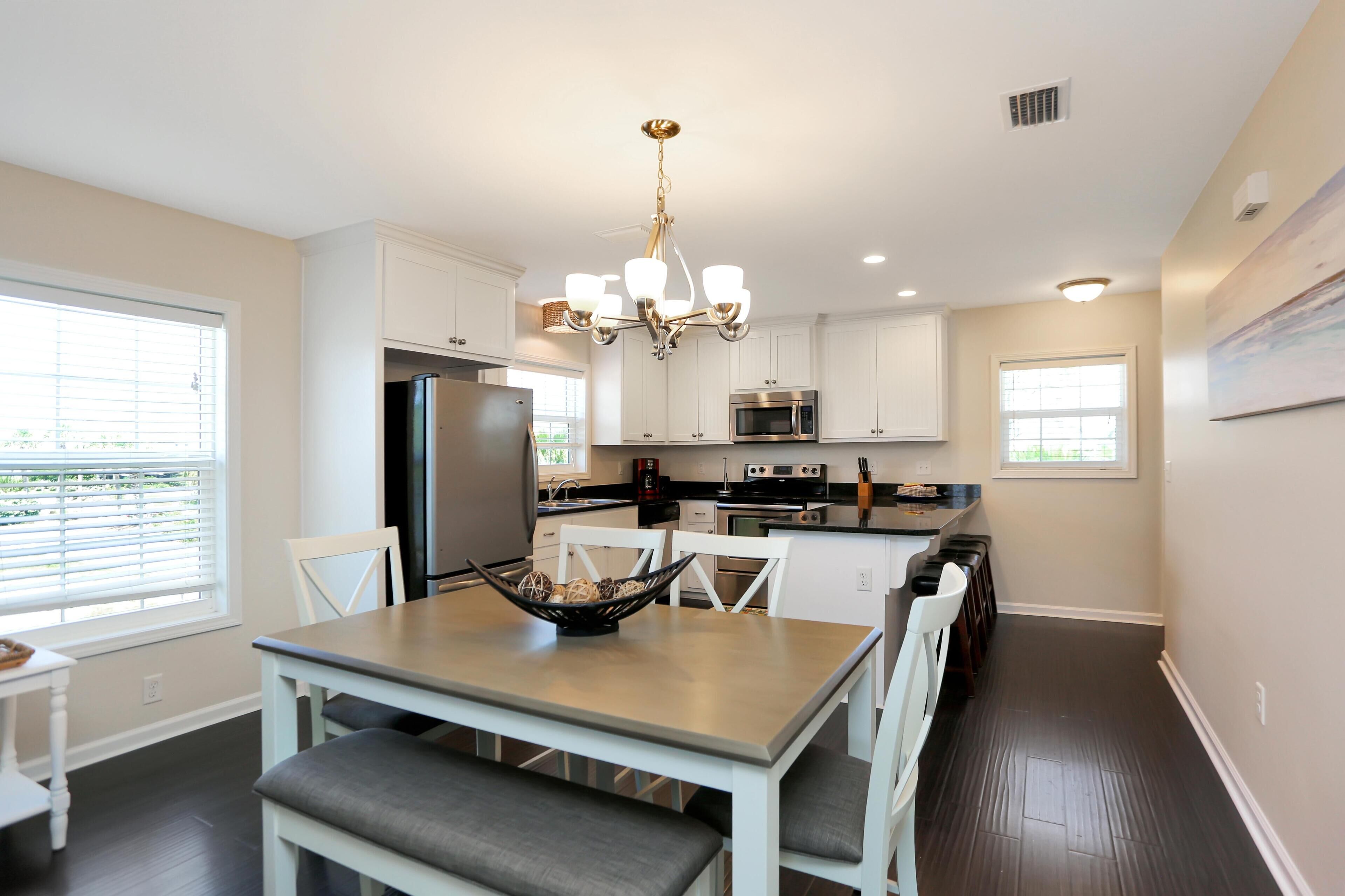 A modern kitchen with white cabinets, a stainless steel refrigerator, a microwave, and a chandelier.