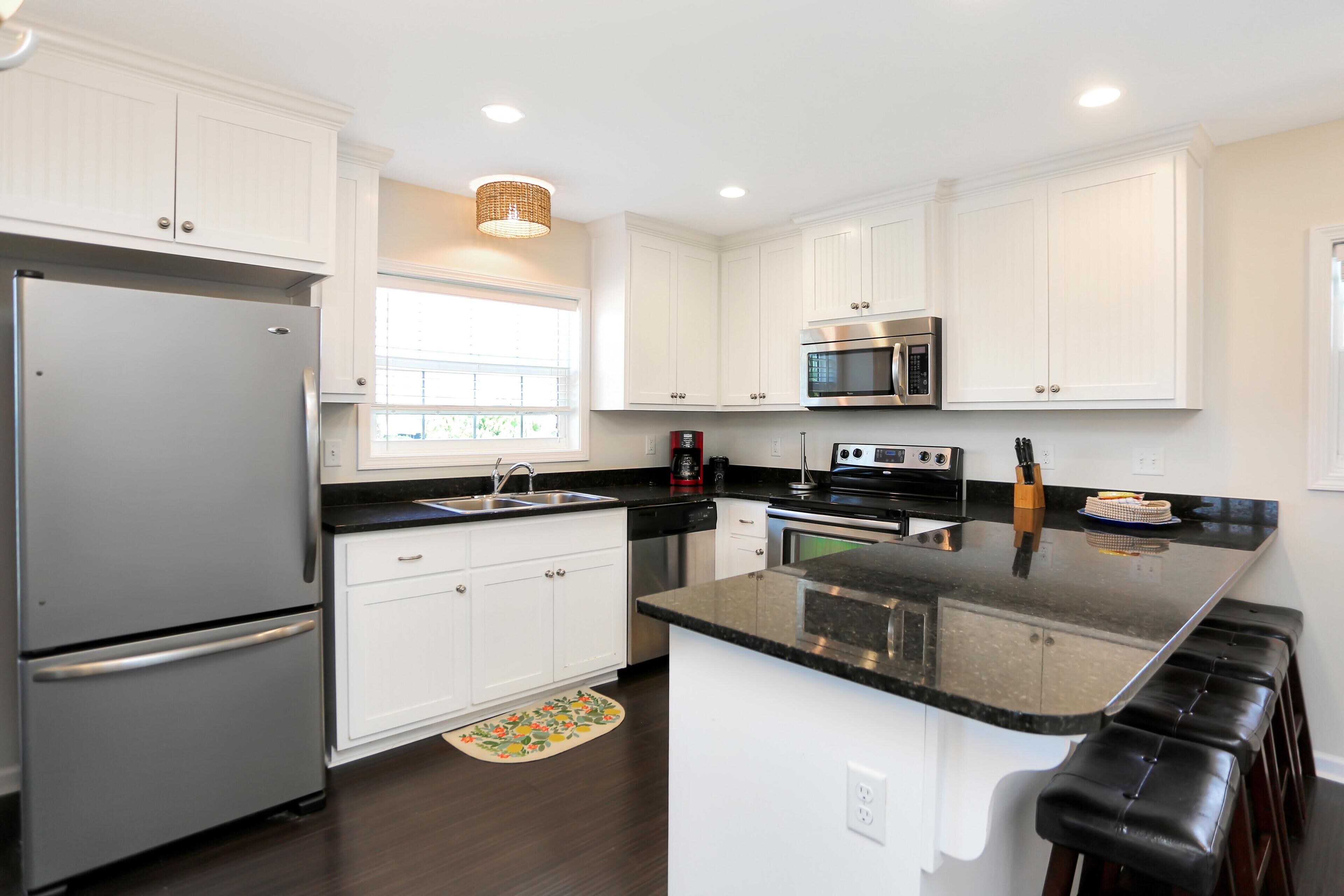 A modern kitchen with white cabinets, stainless steel appliances, a black countertop, and a window providing natural light.