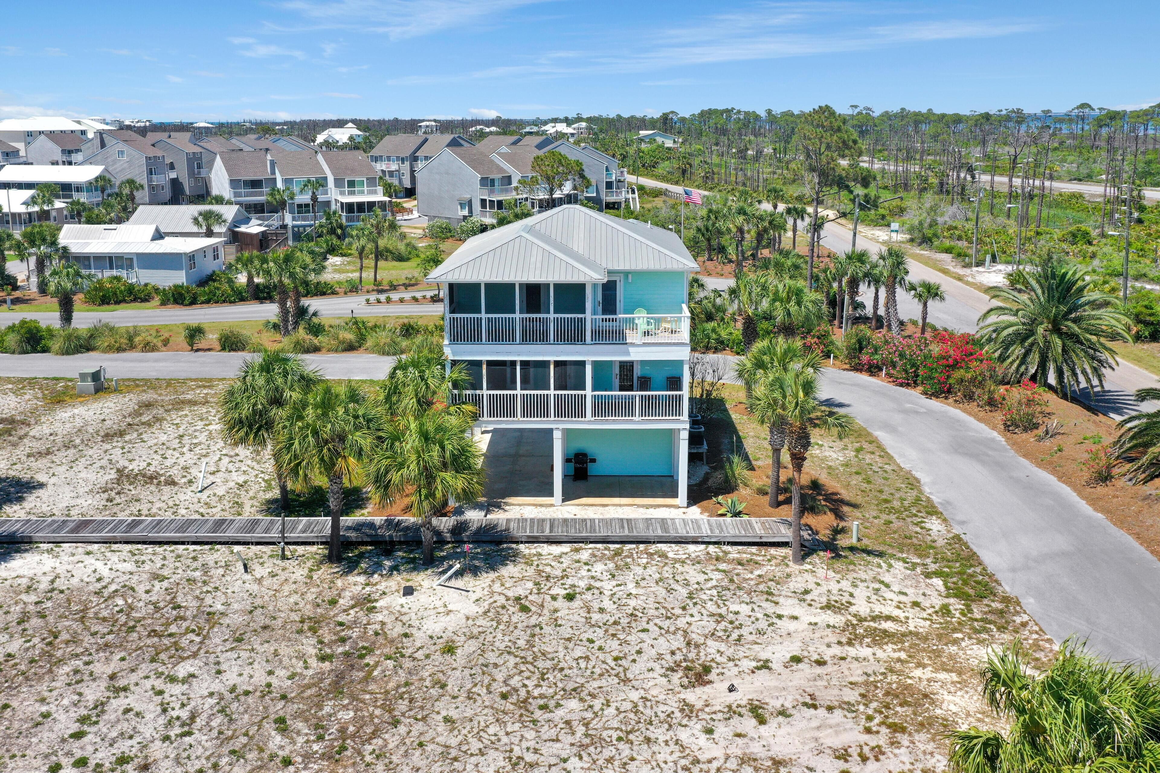 A two-story beachfront house with a balcony, surrounded by palm trees and a sandy beach.