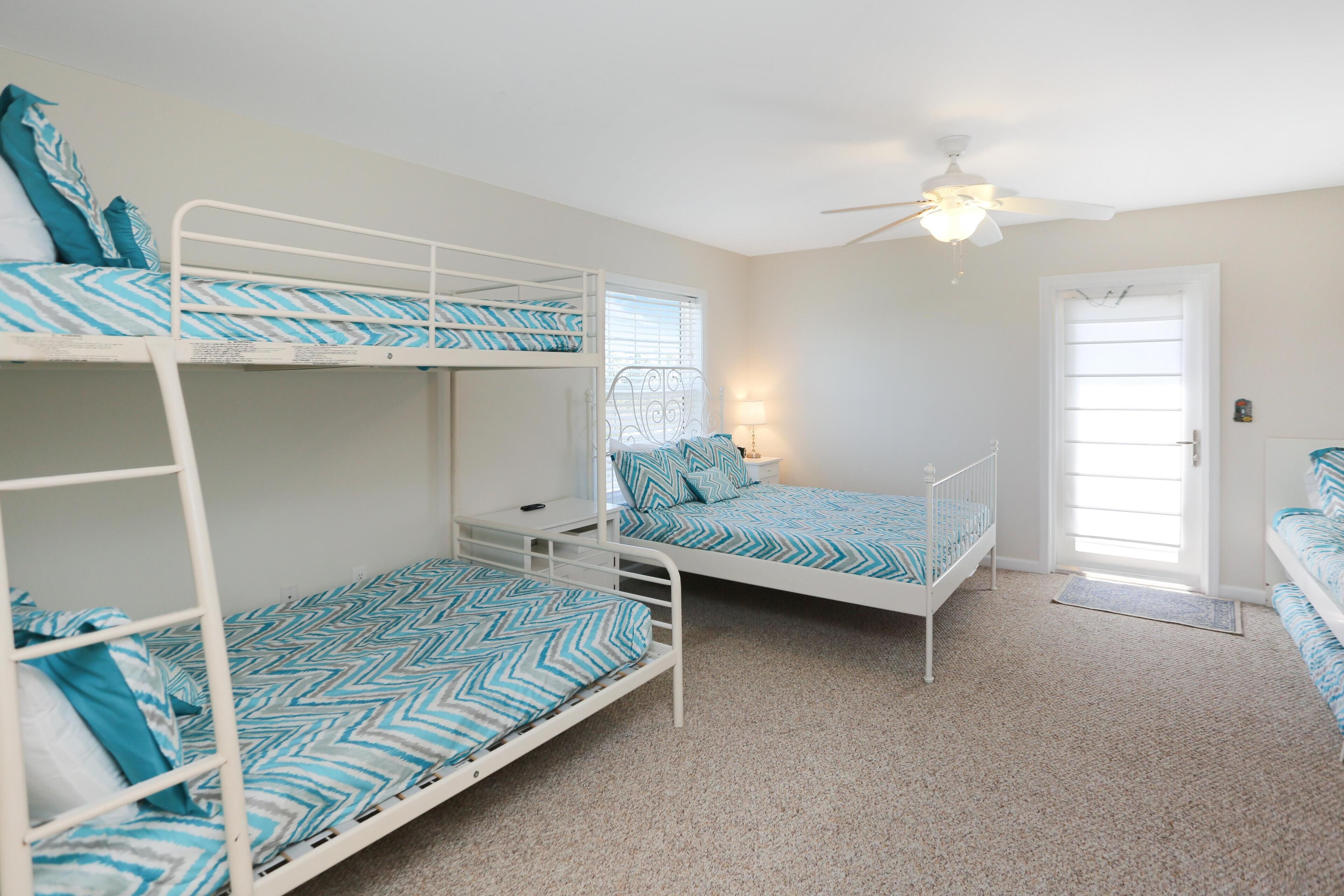 A room with bunk beds, a ceiling fan, a window with blinds, and a door.