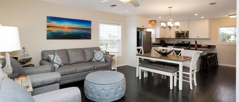 A modern living room with a gray sofa, ottoman, and dining table with chairs.