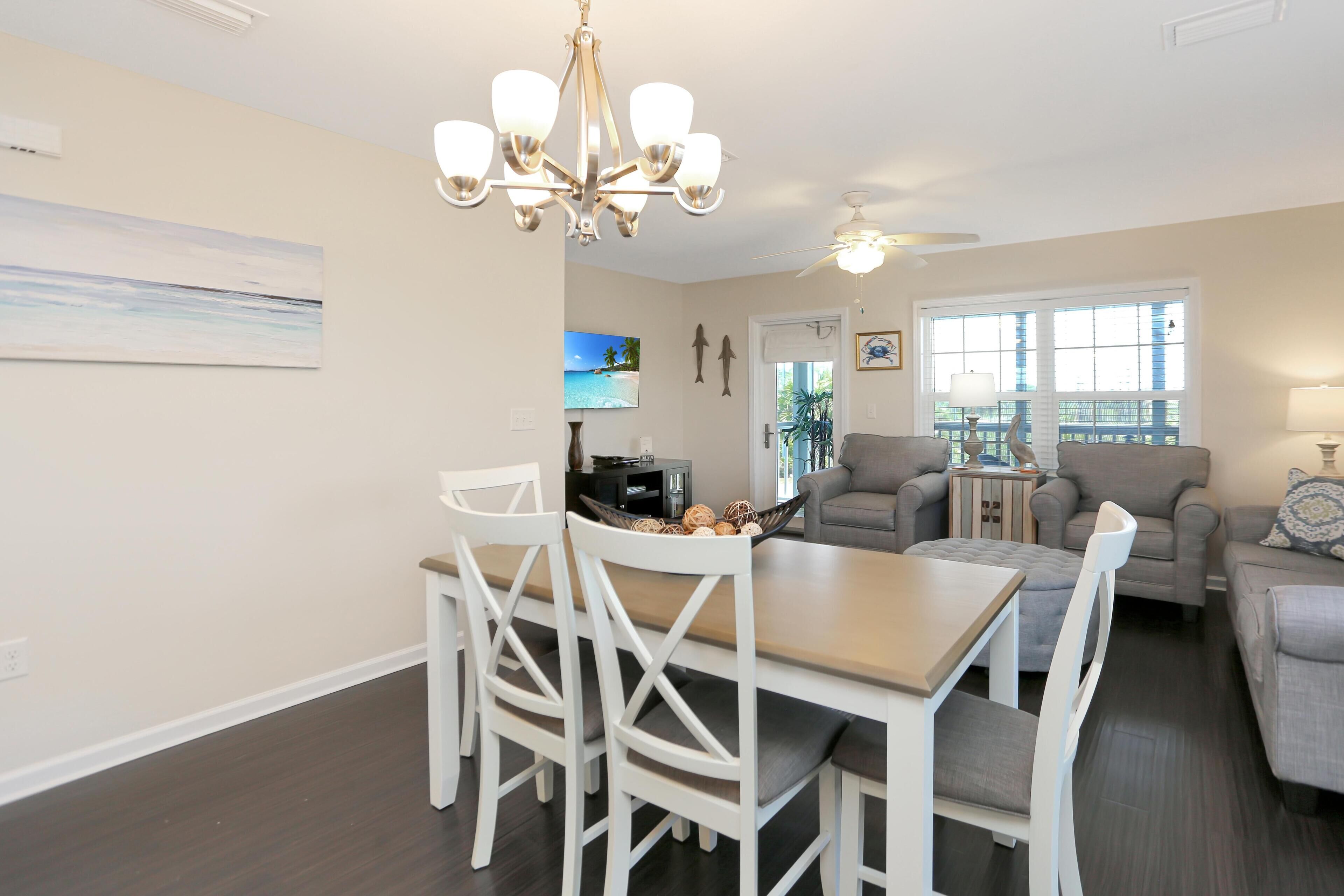A modern living room with a dining area, a ceiling fan, and a large window with a view.