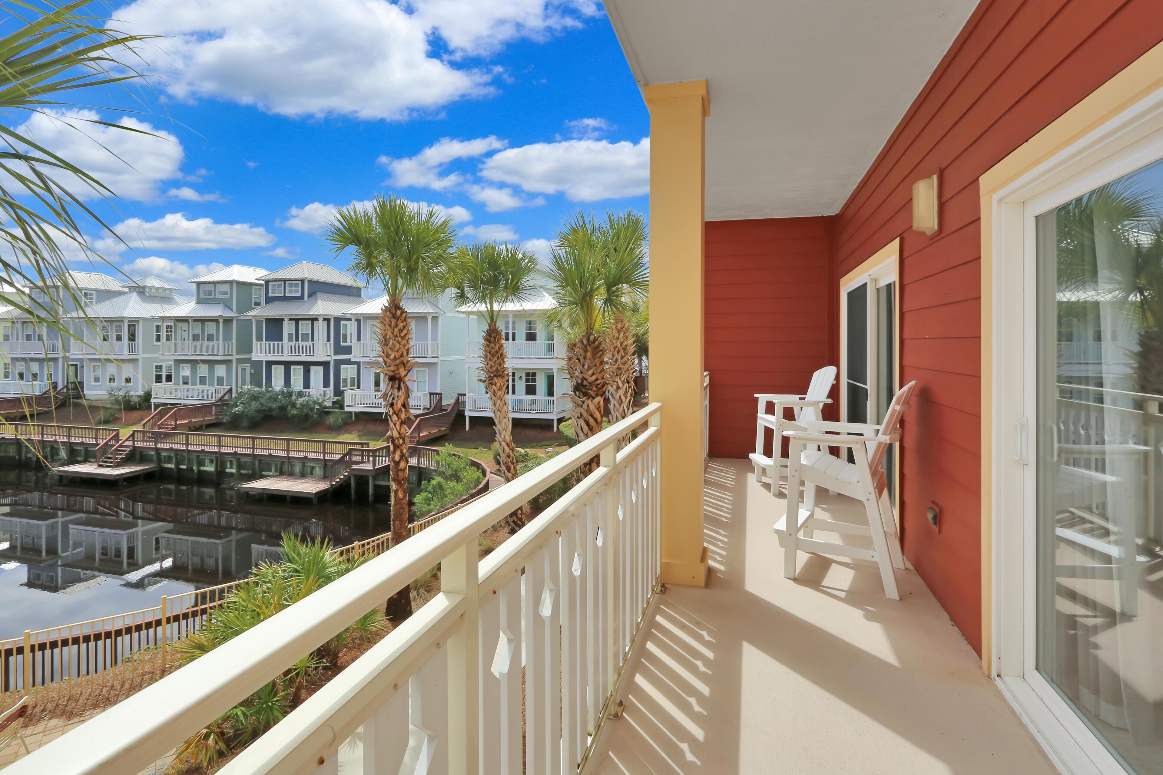 A balcony with white chairs, a view of a water body, and buildings in the background.