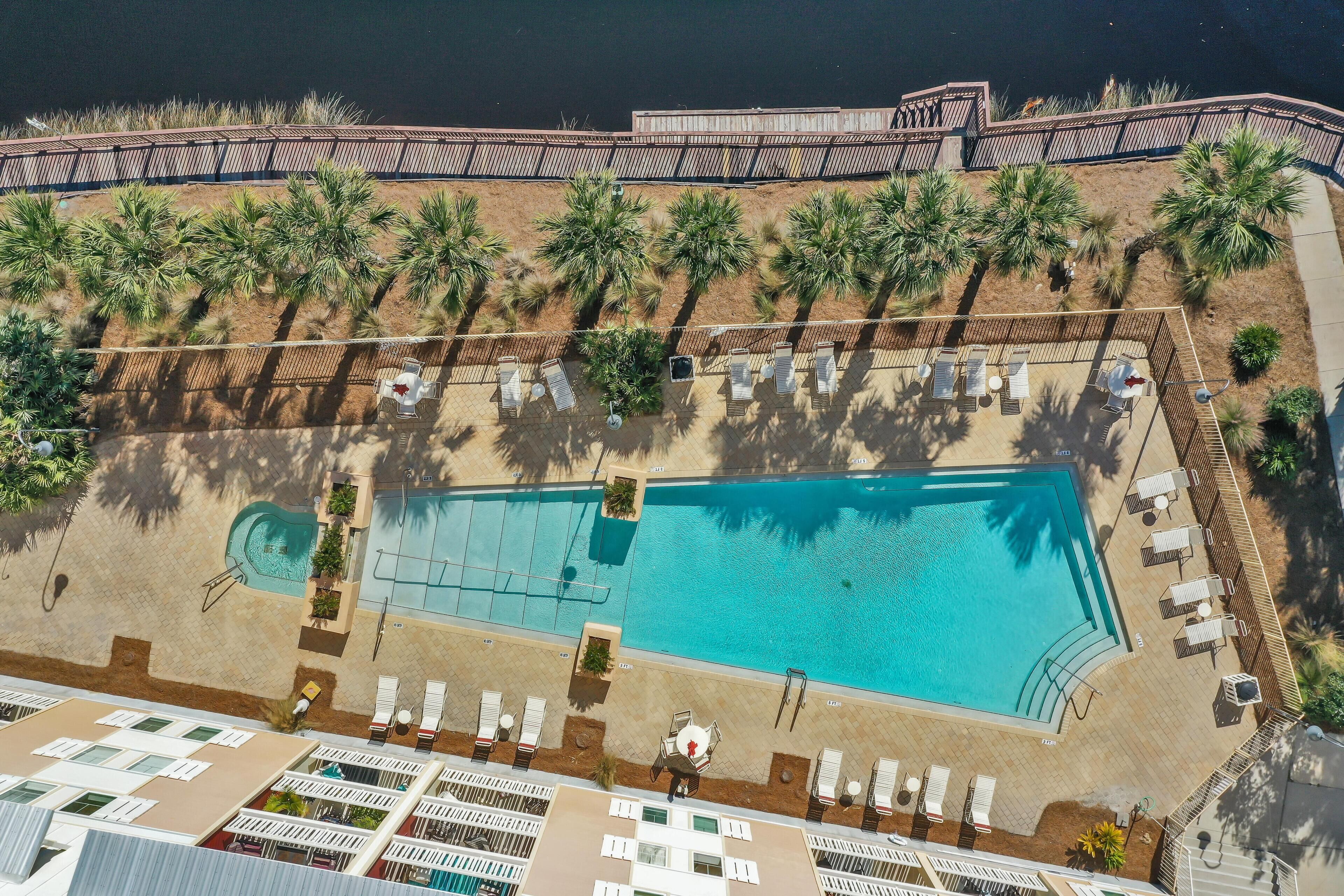 Vista aérea de un resort con piscina, palmeras y tumbonas.