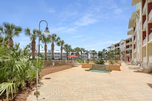Un patio de resort con palmeras, mobiliario exterior y una piscina.