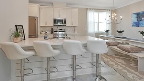 A modern kitchen with white cabinets, stainless steel appliances, and a central island with bar stools. - Just Beach Baby! (Port St. Joe)