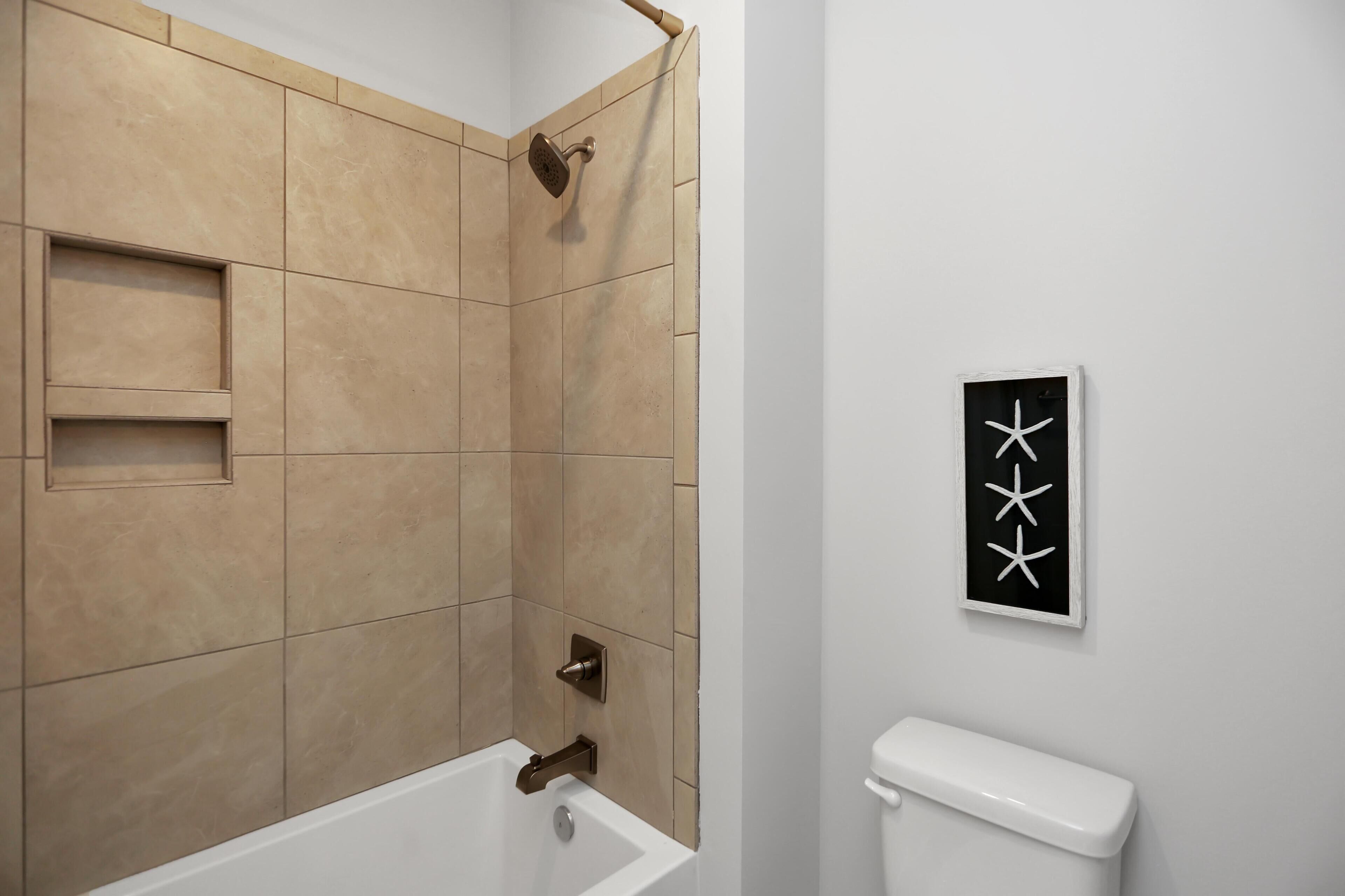 Ein Badezimmer mit beigen Fliesen, einer weißen Toilette und einem gerahmten Kunstwerk an der Wand.