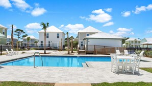 A swimming pool with a wooden deck, white lounge chairs, and a fenced area with palm trees. - Just Beach Baby! (Port St. Joe)