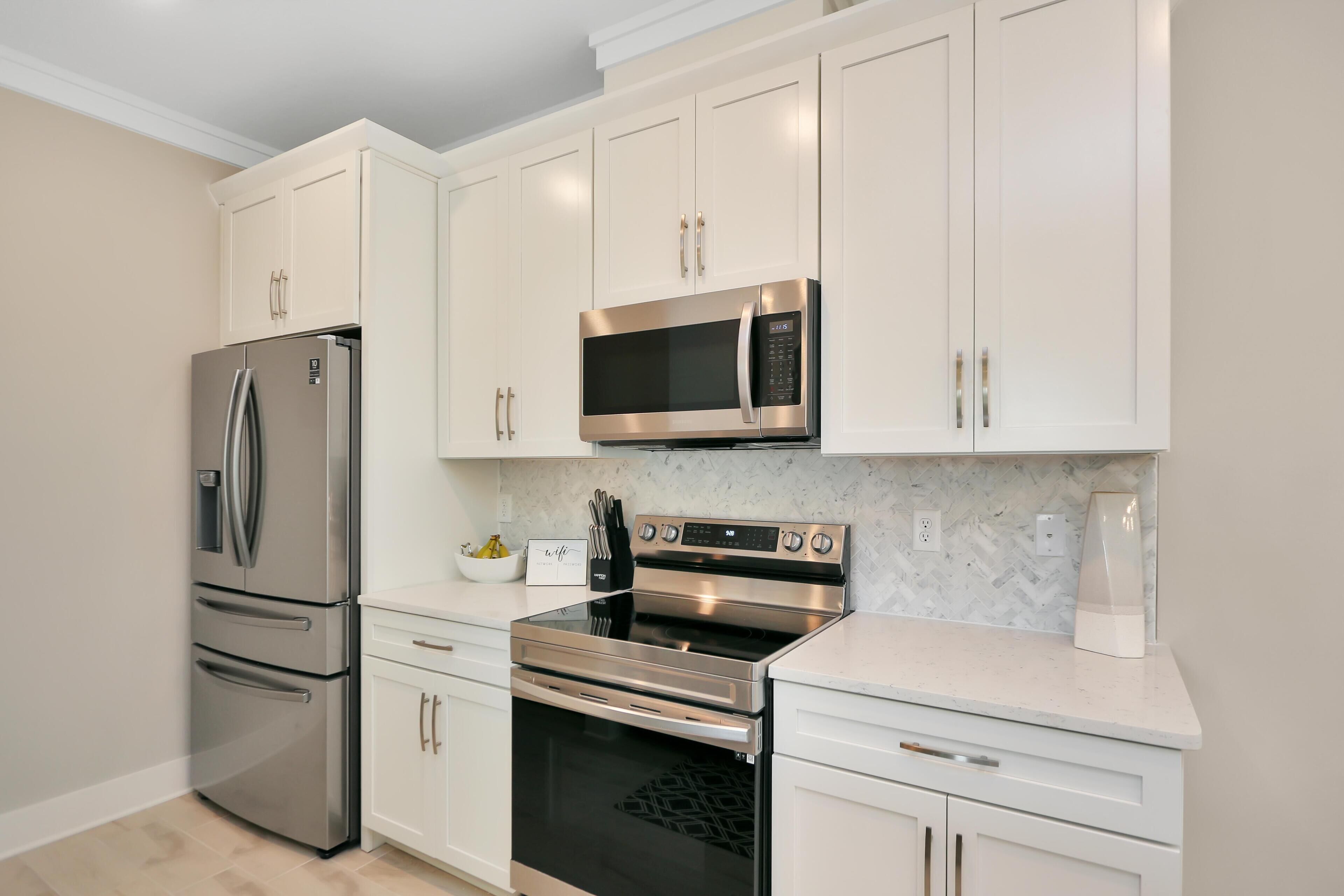A modern kitchen with stainless steel appliances, white cabinetry, and a marble backsplash.