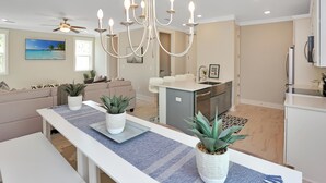 A modern kitchen with a central island, a dining area with a long table, and a living room with a sofa and a ceiling fan. - Just Beach Baby! (Port St. Joe)