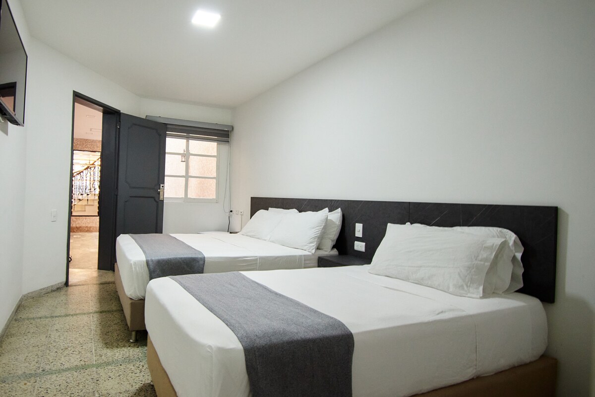 Ein Hotelzimmer mit zwei Betten, einer Tür, die auf einen Balkon führt, und einem kleinen Fenster.