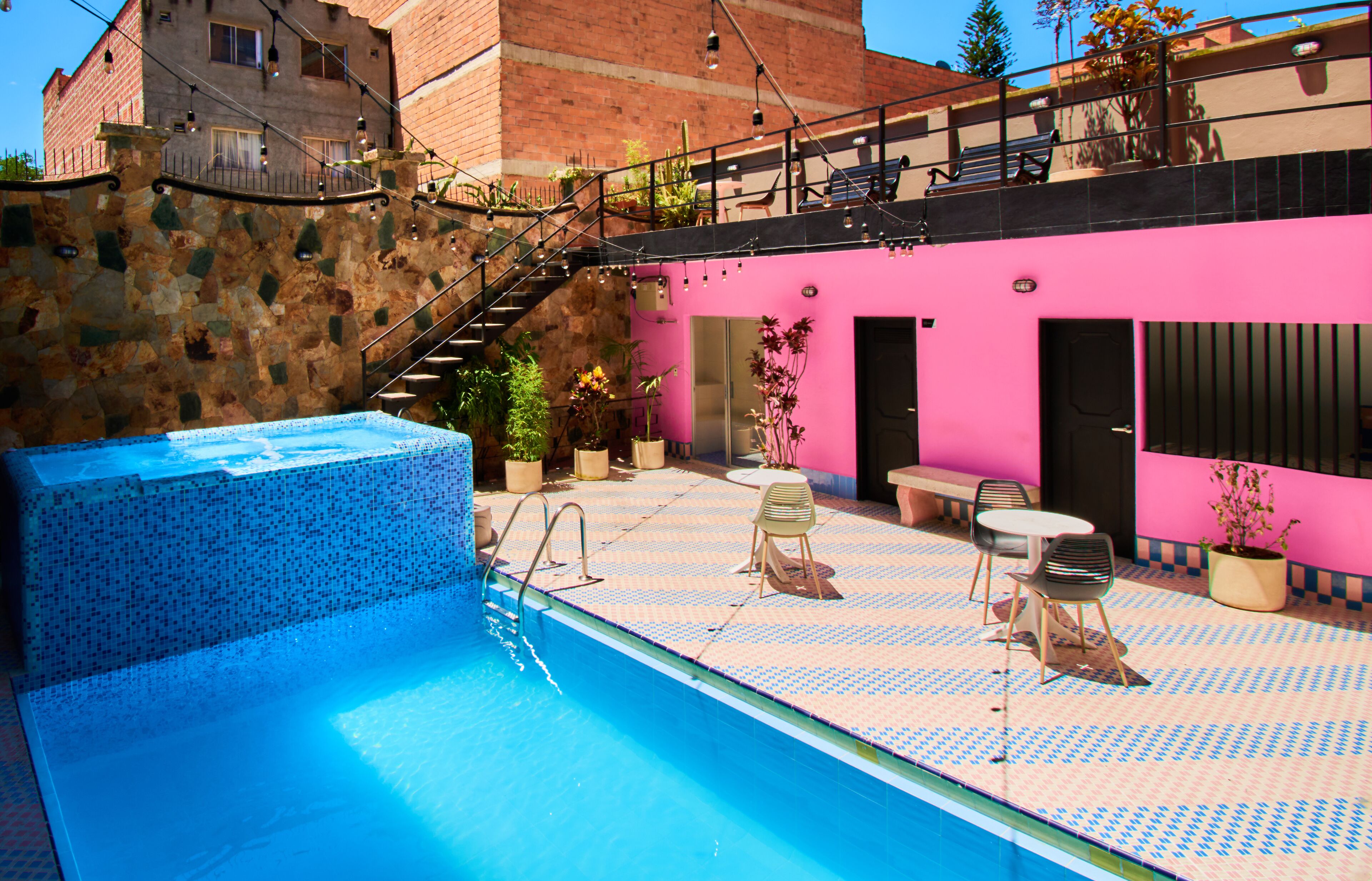 Une piscine avec un mur en pierre et un bâtiment rose en arrière-plan.