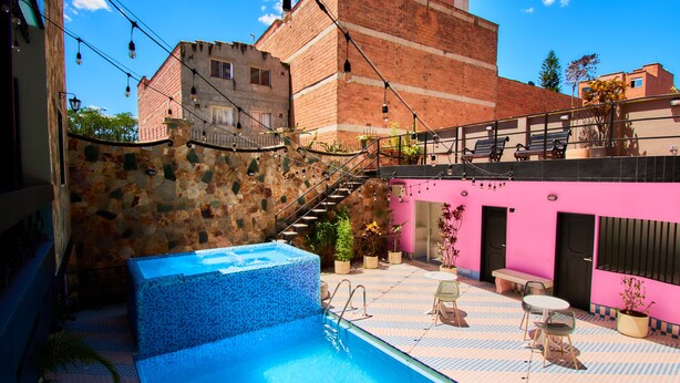 Un área de piscina en la azotea con un muro de piedra, una escalera y un edificio rosa al fondo.