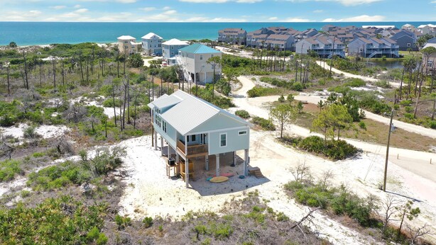 A beachfront property with a single-story house featuring a balcony, a sandy driveway, and a view of the ocean. - Cape Bear (Port St. Joe)