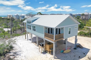 A beach house with a balcony, a small deck, and a sandy beach area with surfboards. - Cape Bear (Port St. Joe)
