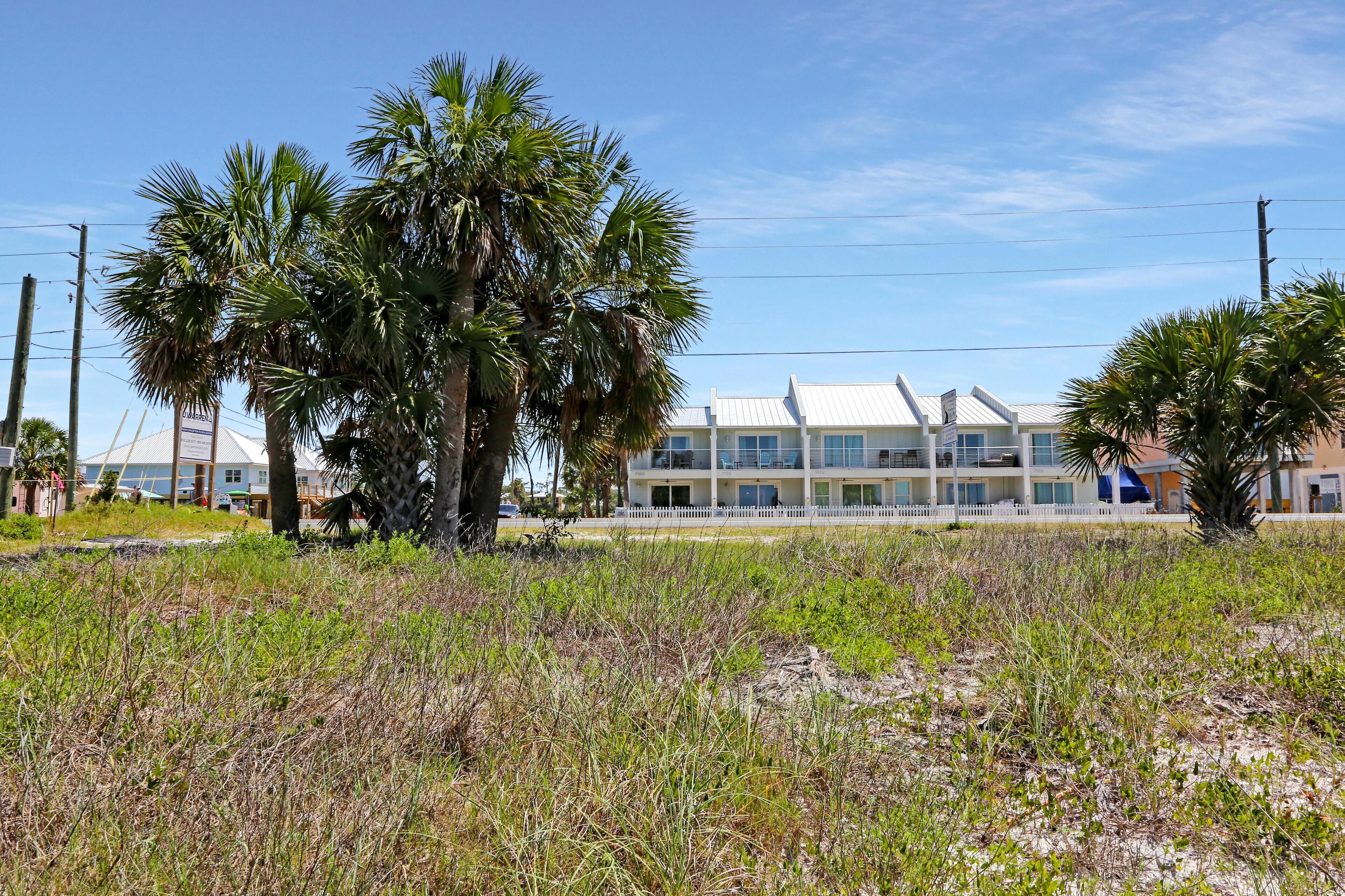 Un hotel frente a la playa con fachada blanca, varios balcones y palmeras en primer plano.