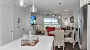 A modern kitchen with a dining area, white cabinetry, and a view of the ocean. - Wine Down (Port St. Joe)