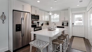 A modern kitchen with white cabinetry, stainless steel appliances, and a central island with bar stools. - Wine Down (Port St. Joe)