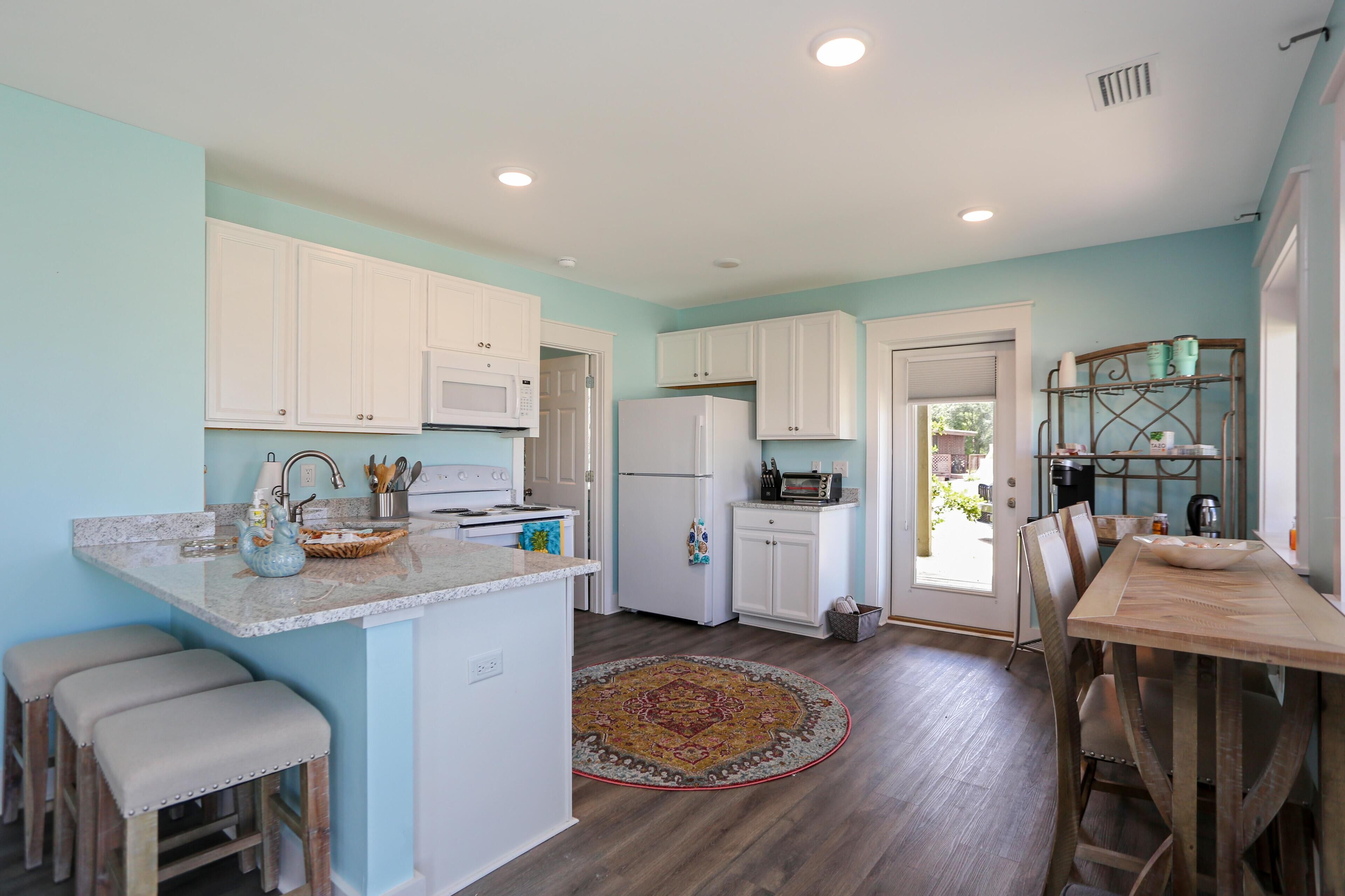 A kitchen with white cabinets, a microwave, a refrigerator, and a dining area with a wooden table and chairs.