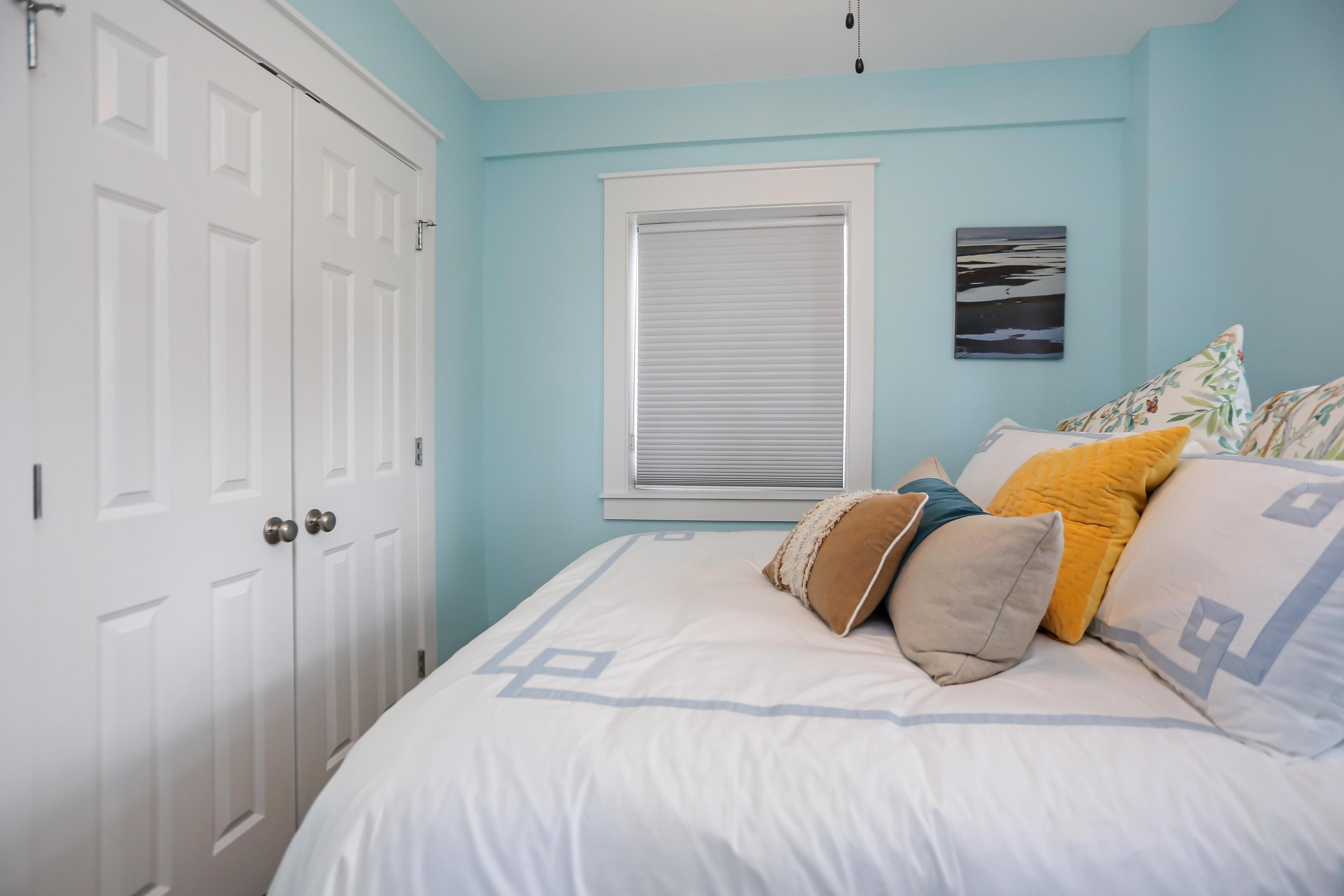 A bedroom with a bed, a window with blinds, a door, and a wall-mounted picture.
