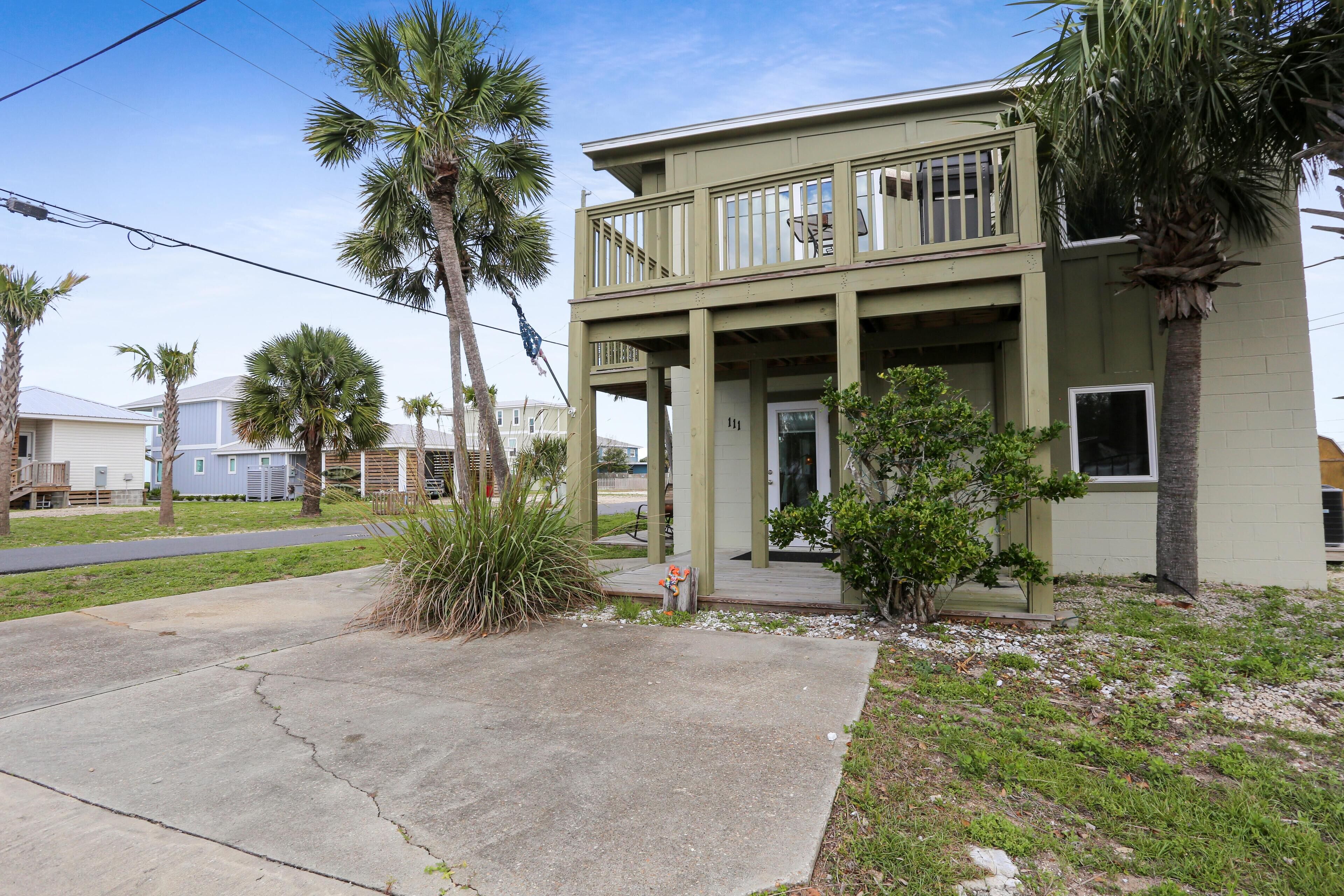 A two-story building with a balcony, surrounded by palm trees and a grassy area.