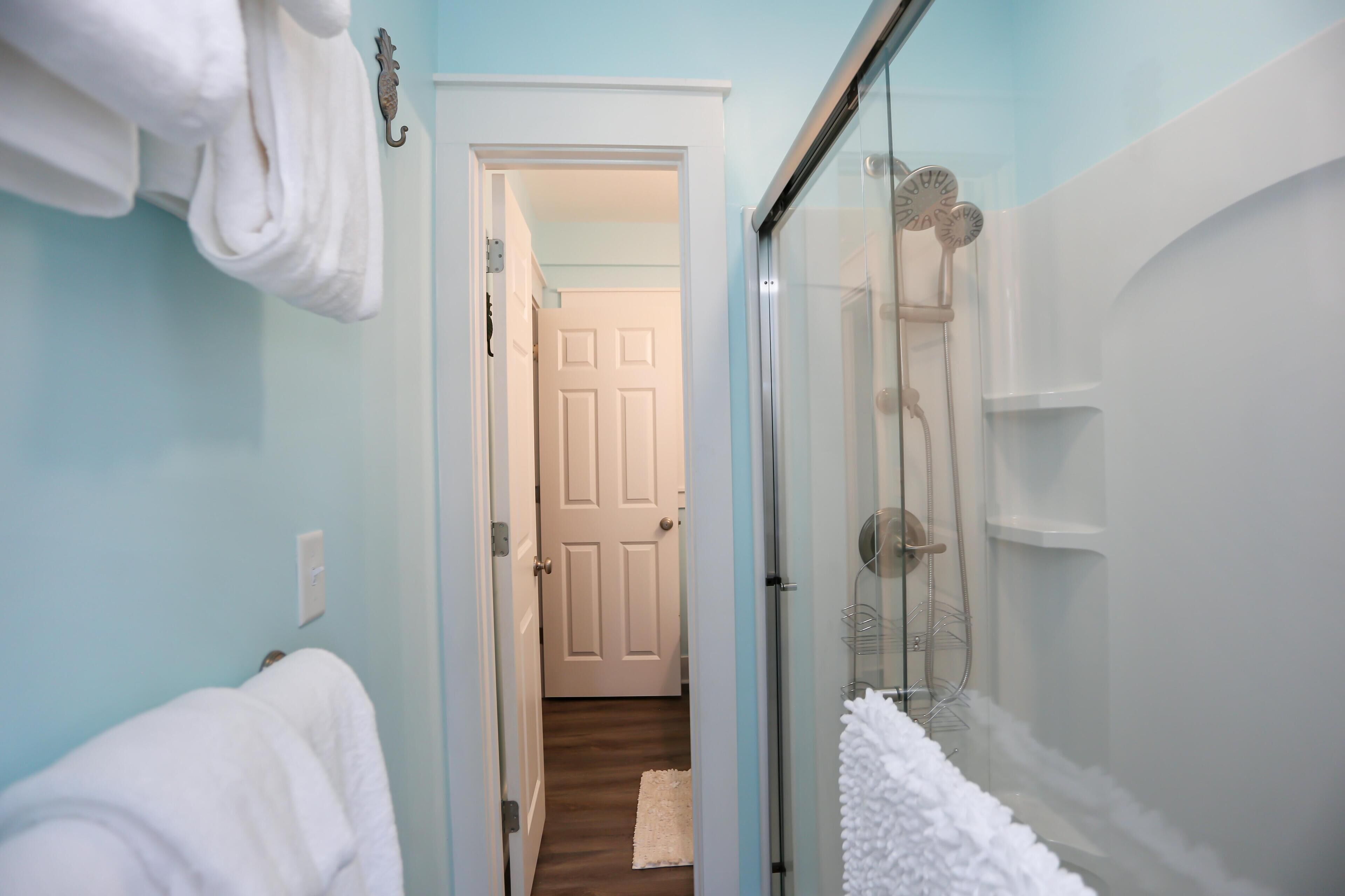A bathroom with a glass shower enclosure, white towels, and a visible door leading to another room.