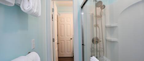 A bathroom with a glass shower enclosure, white towels, and a visible door leading to another room.