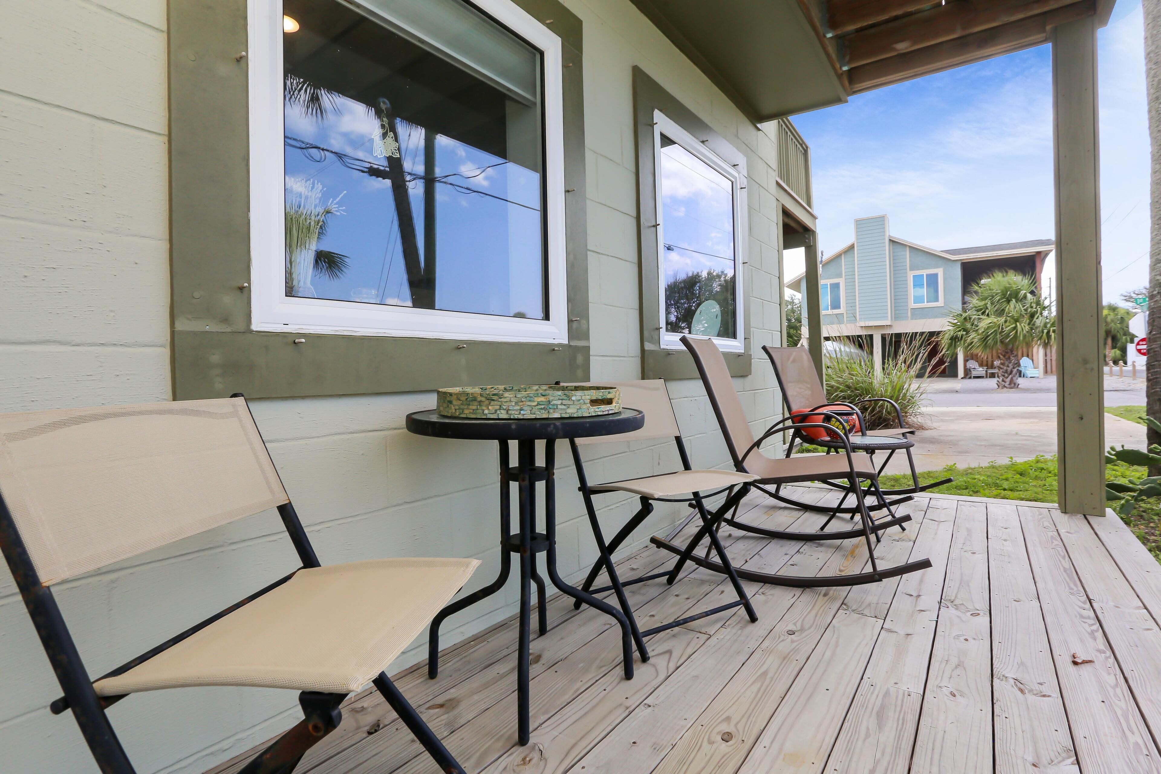 A wooden deck with two chairs and a small table, a covered porch, and a view of a house in the background.