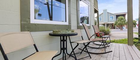 A wooden deck with two chairs and a small table, a covered porch, and a view of a house in the background.