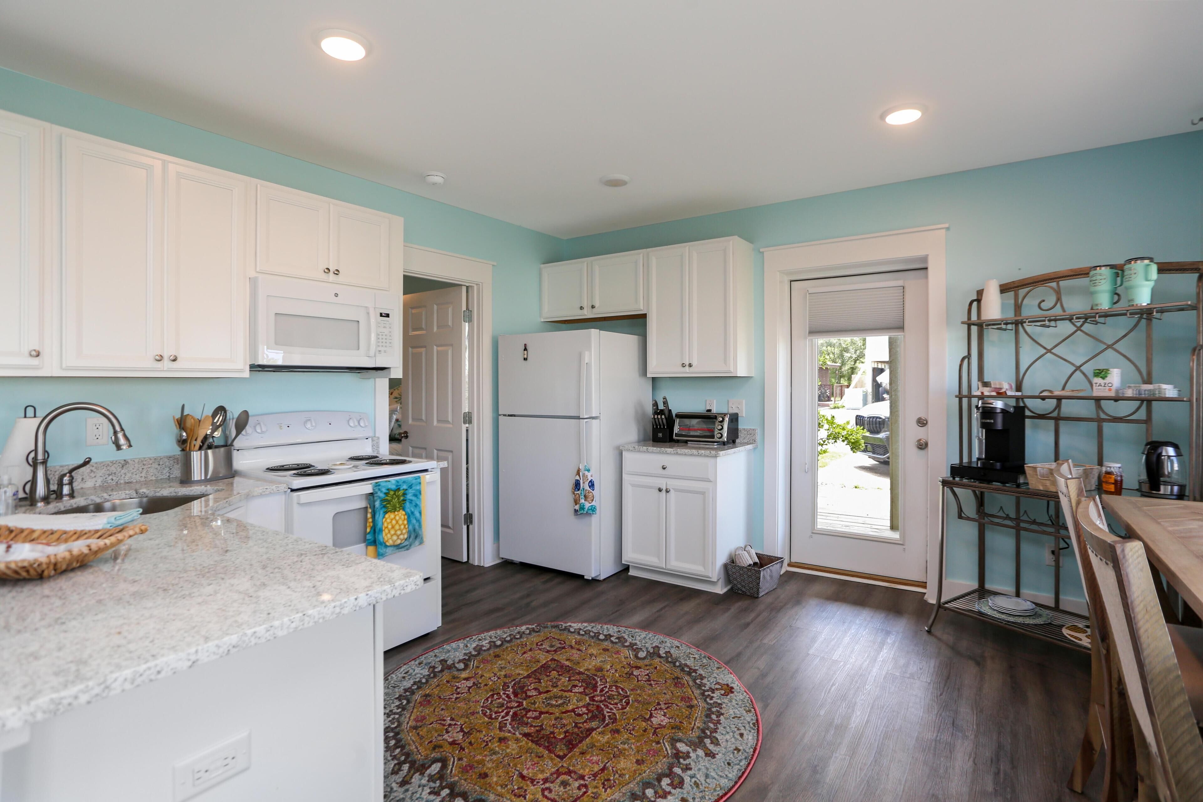 Una cocina con armarios blancos, microondas, refrigerador, estufa y un comedor con mesa y sillas.