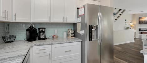 A modern kitchen with white cabinets, a stainless steel refrigerator, and a marble countertop.