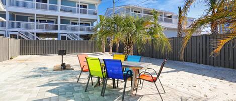 A patio with a table and chairs, a wooden fence, and a building with balconies in the background.