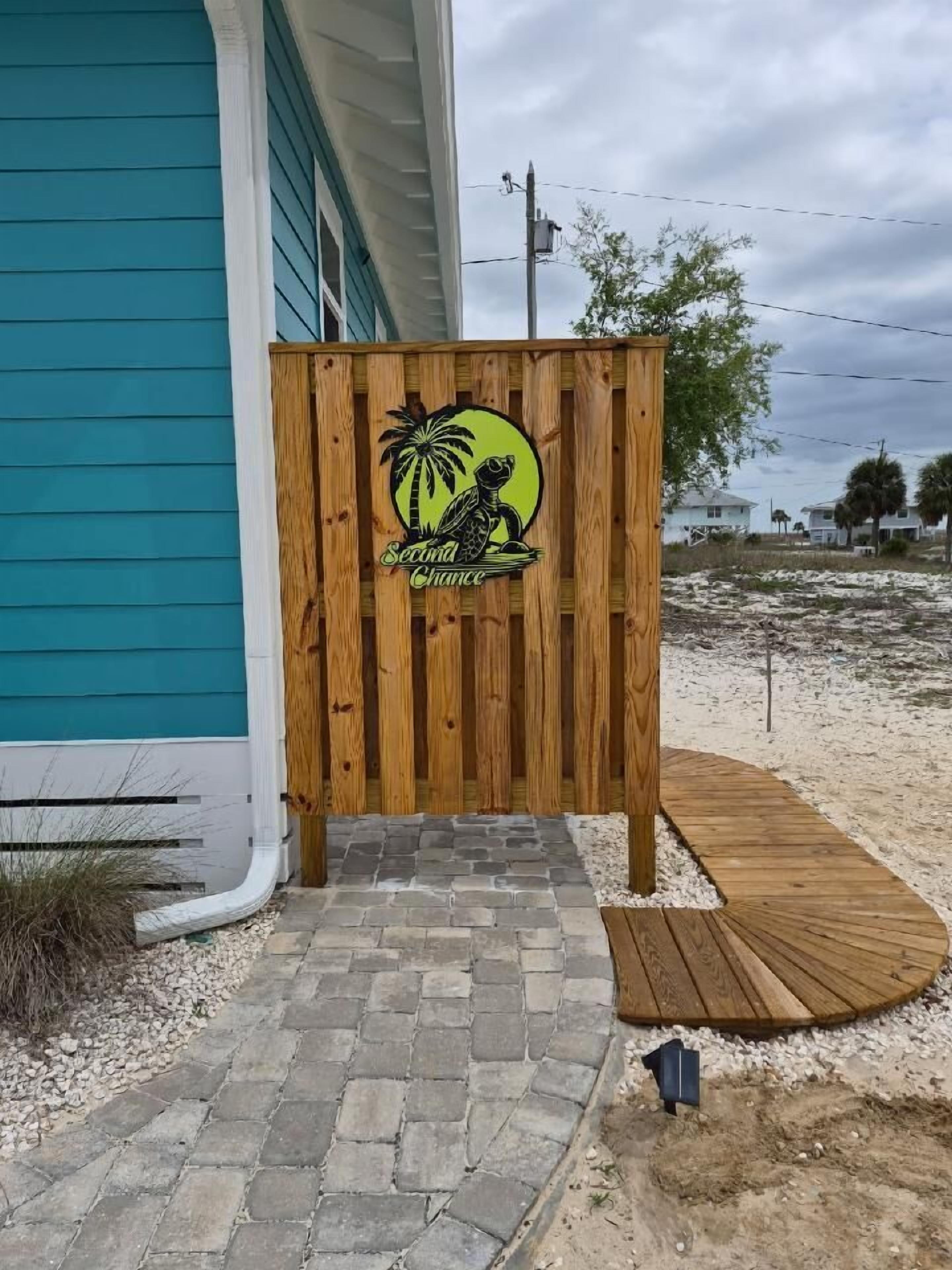 A wooden fence with a logo, a paved pathway, and a house with teal siding.