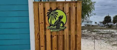 A wooden fence with a logo, a paved pathway, and a house with teal siding.