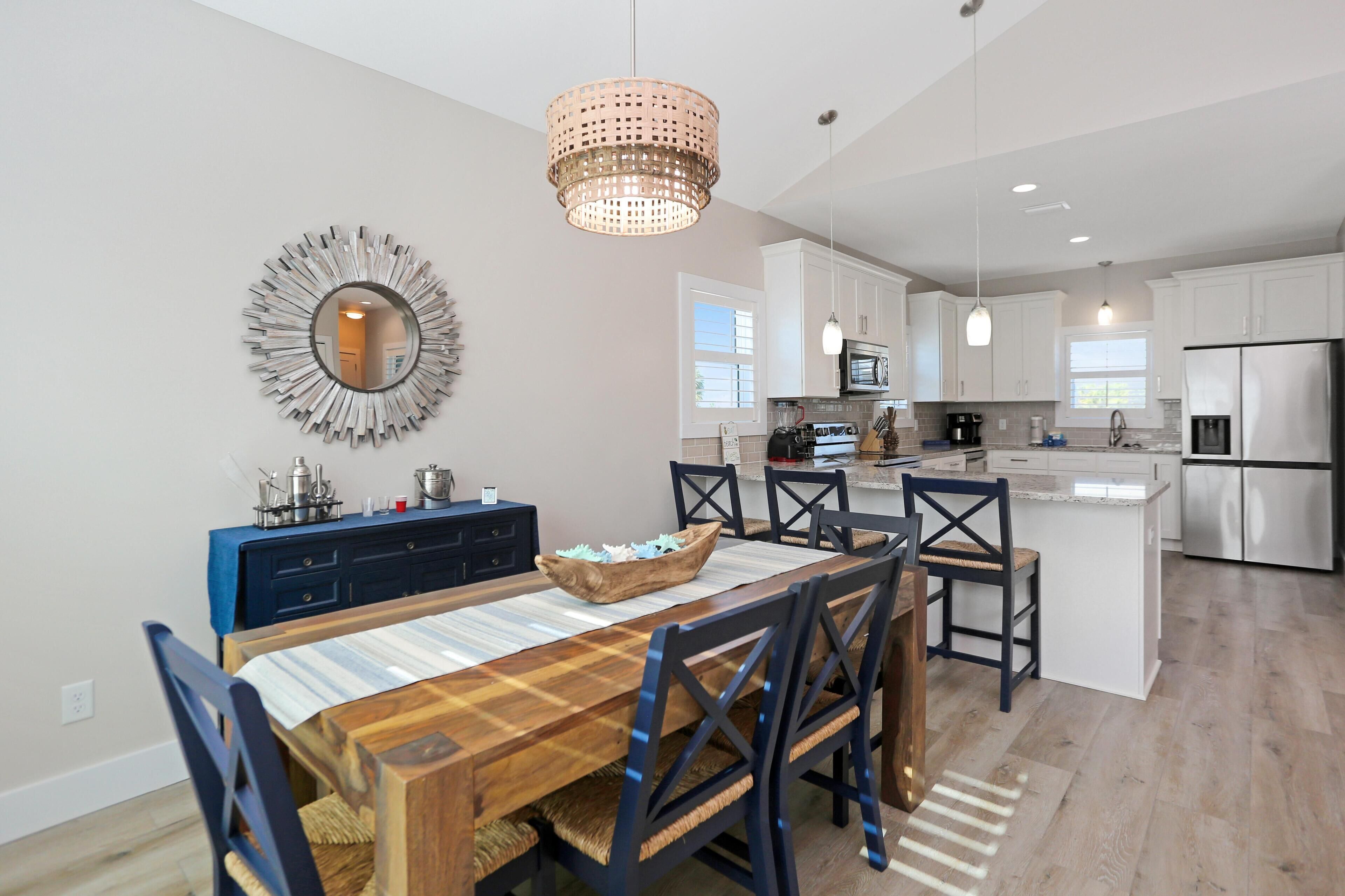 A modern kitchen with white cabinets, a central island, and a dining area with a wooden table and chairs.