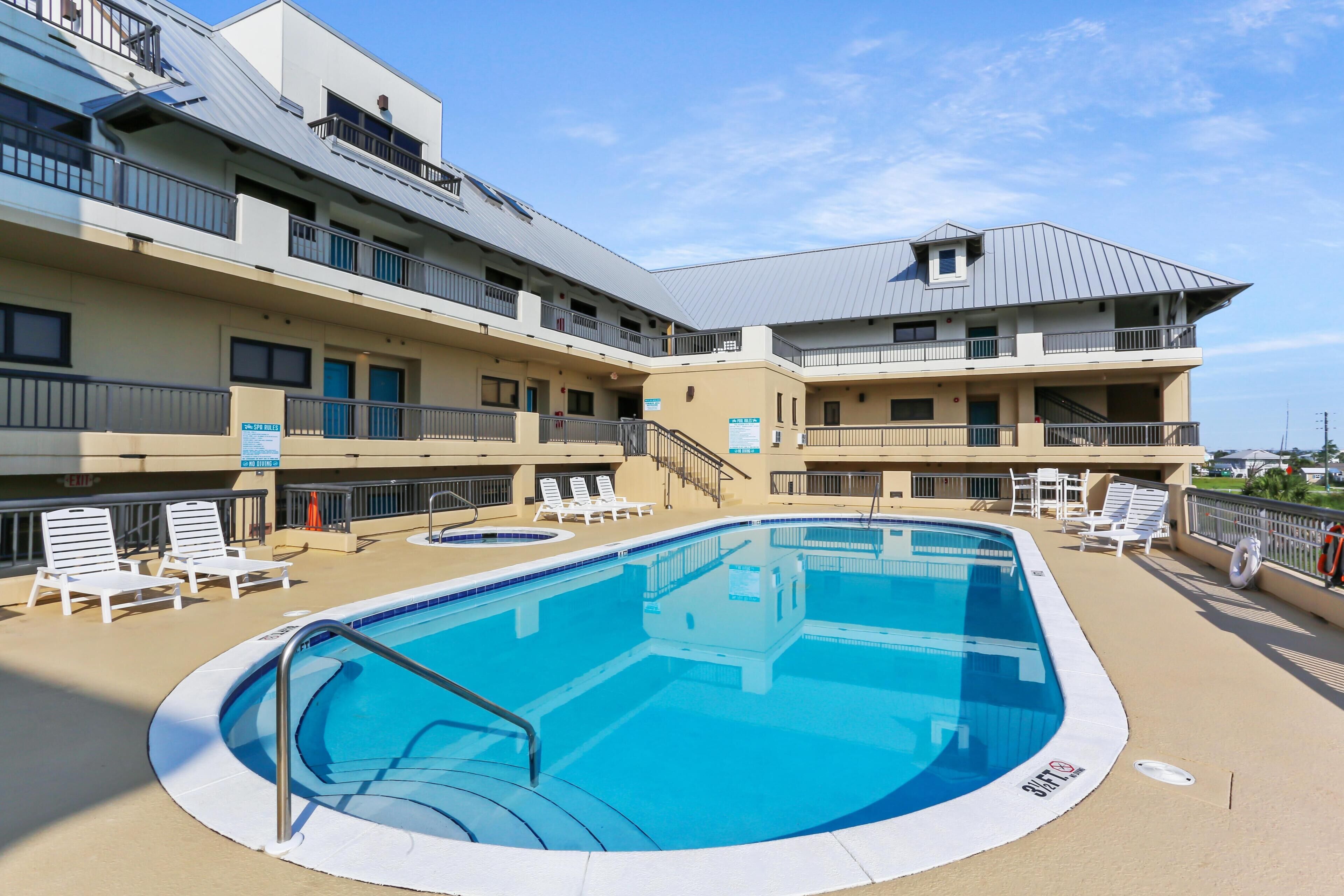 A swimming pool with lounge chairs and a building with balconies.