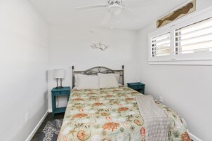 Quarto com cama, mesa de cabeceira, luminária, ventilador de teto e janela com persianas.